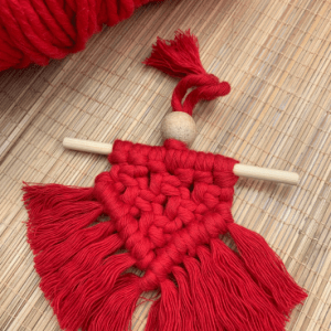 Handcrafted red mini macramé wall hanging with fringe, wooden bead, and hanging rod