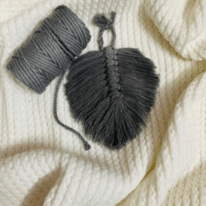 Handcrafted mini macramé leaf wall hanging in charcoal grey cotton, with soft textured fringe and central spine