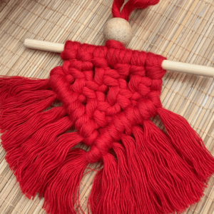 Handcrafted red mini macramé wall hanging with fringe, wooden bead, and hanging rod