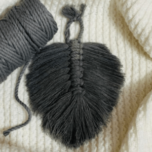 Handcrafted mini macramé leaf wall hanging in charcoal grey cotton, with soft textured fringe and central spine