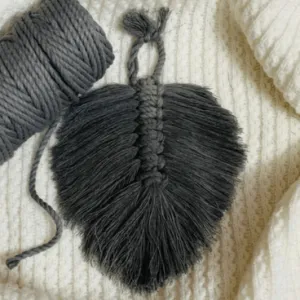 Handcrafted mini macramé leaf wall hanging in charcoal grey cotton, with soft textured fringe and central spine